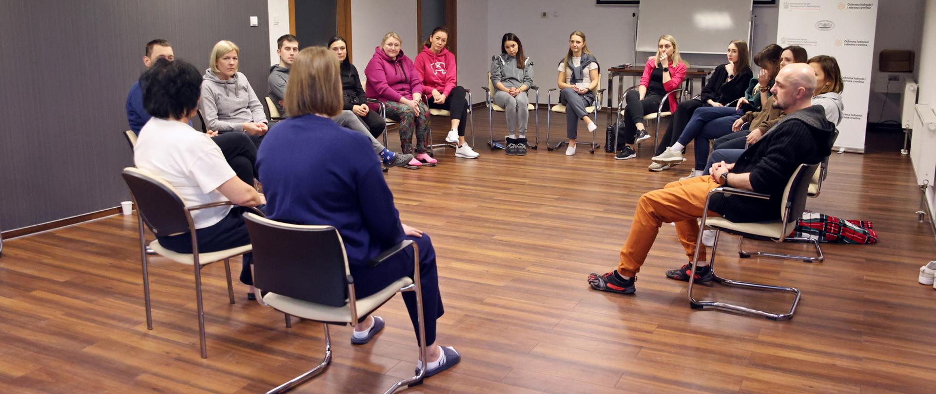 Uczestnicy warsztatów siedzący w sali konferencyjnej na krzesłach ustawionych w kształt okręgu podczas zajęć