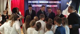 Elegancko ubrane dzieci stoją w grupie i rozmawiają z dorosłymi, wśród których jest minister Czarnek.