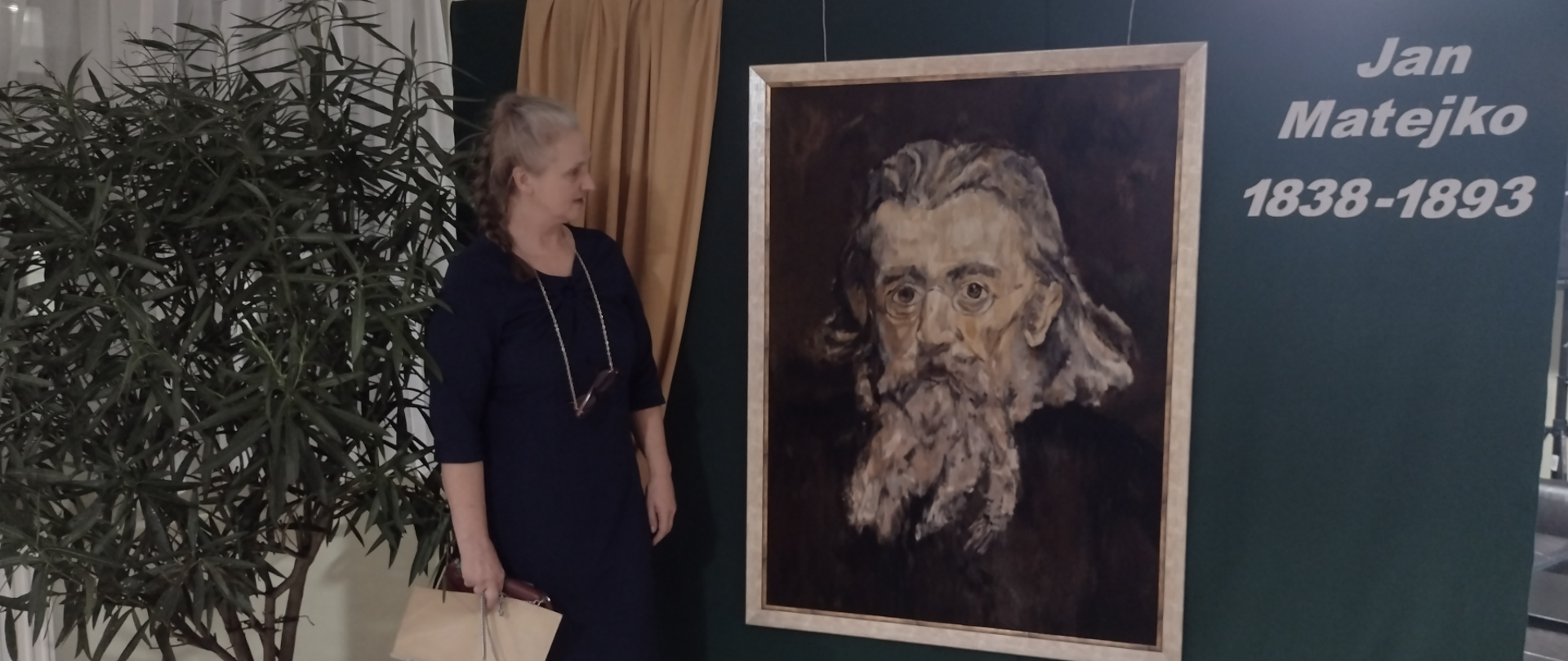 fotografia barwna: kobieta-prelegentka obok planszy z portretem Matejki i napisem: Jan Matejko 1838-1893