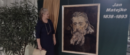 fotografia barwna: kobieta-prelegentka obok planszy z portretem Matejki i napisem: Jan Matejko 1838-1893