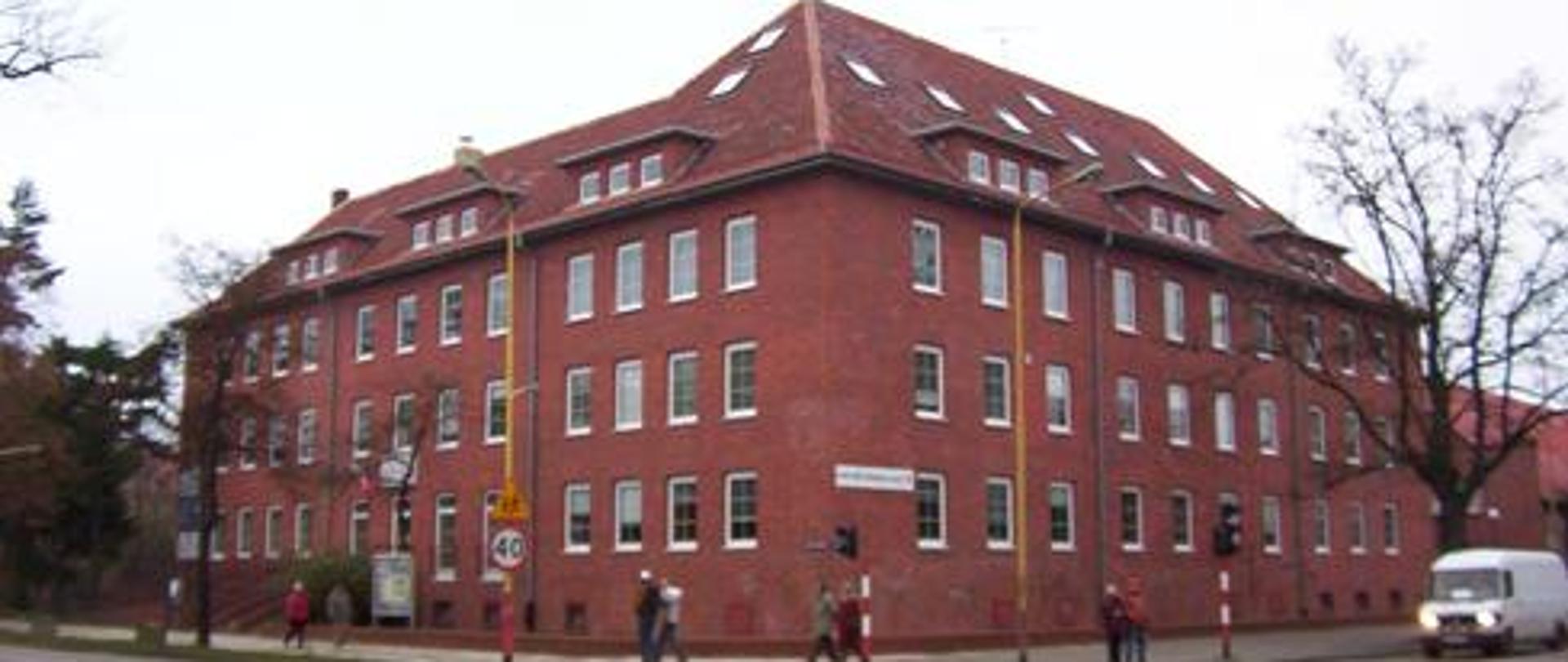 Na zdjęciu budynek szkoły z czerwonej cegły , na rogu skrzyżowania ulic.