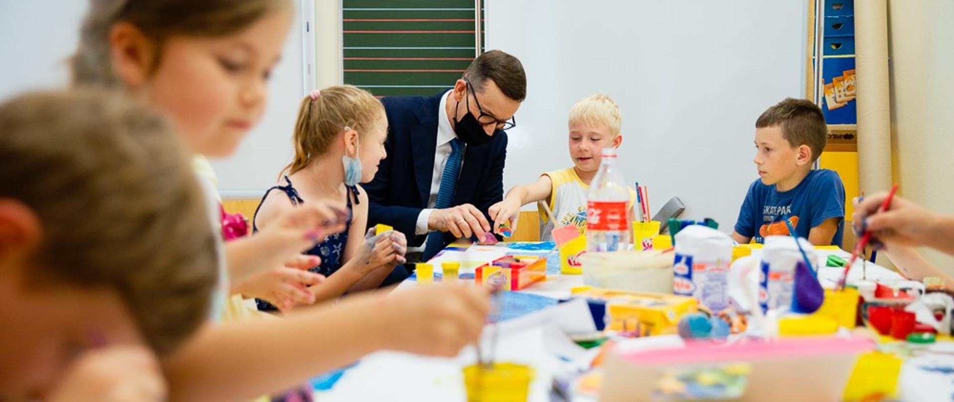 Premier w sali, w której dzieci siedzą przy stole.
