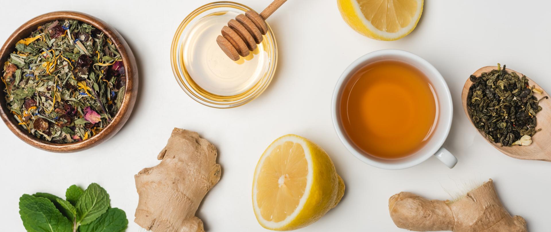 Na zdjęciu jest imbir, miód, cytryna, mięta i zioła. Leżą na stole.