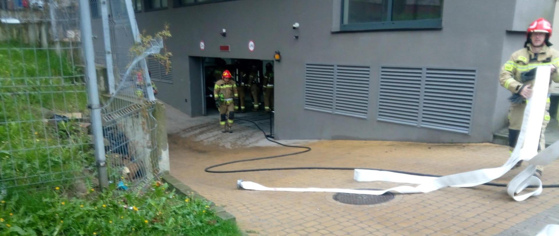 Zdjęcie przedstawia wjazd do garażu podziemnego w budynku przy ulicy Seminaryjskiej w Kielcach gdzie doszło do pożaru. Ratownicy zwijają węże gaśnicze oraz znajdują się wewnątrz obiektu. 