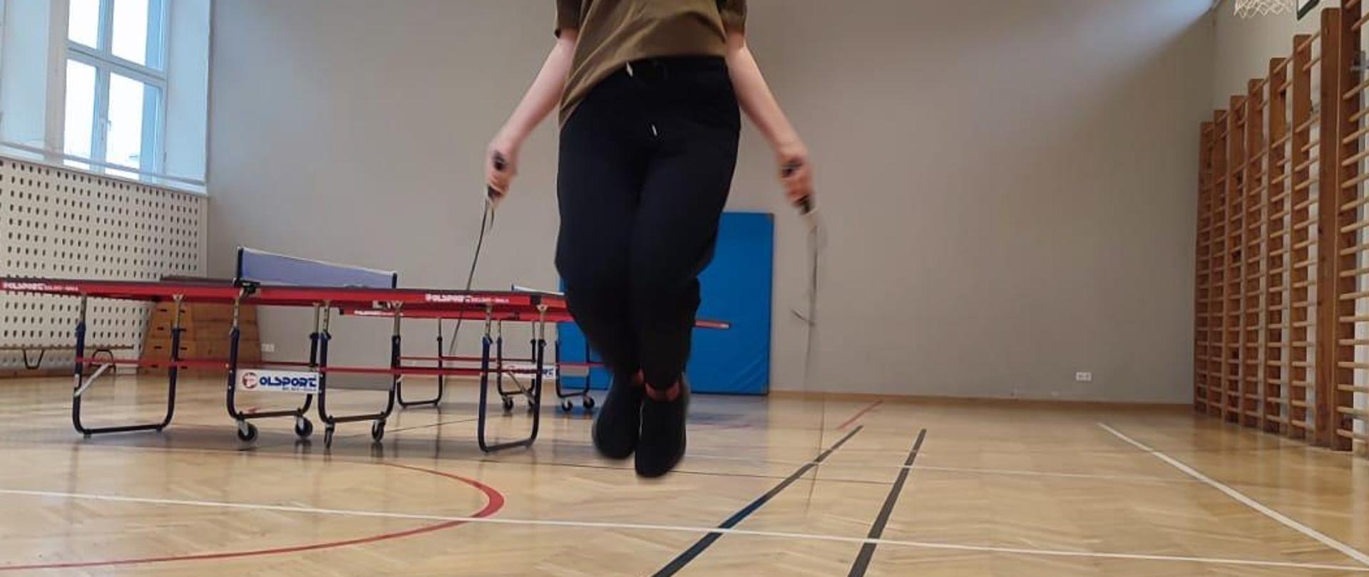 Sala gimnastyczna. Młoda osoba skacze na skakance