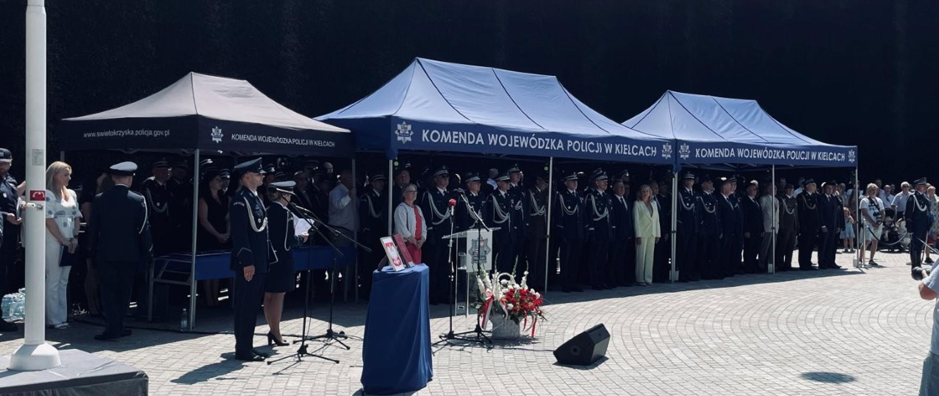 Oficjalni uczestnicy uroczystości Obchodów Święta Policji stojący pod namiotem podczas oficjalnej części uroczystości.