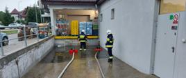 Strażacy OSP nadzorujący motopompy pływające wypompowują wodę z podjazdu rampy załadunkowej w sklepie wielkopowierzchniowym.