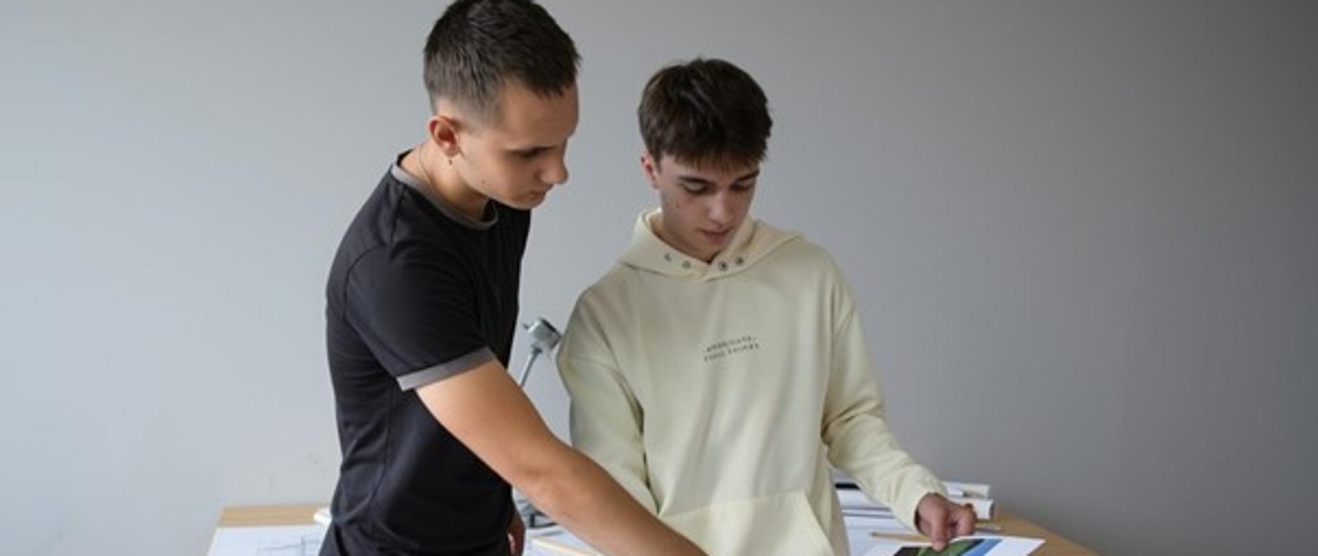 Dwóch uczniów przeglądających projekt ogrodu, na biurku inne projekty