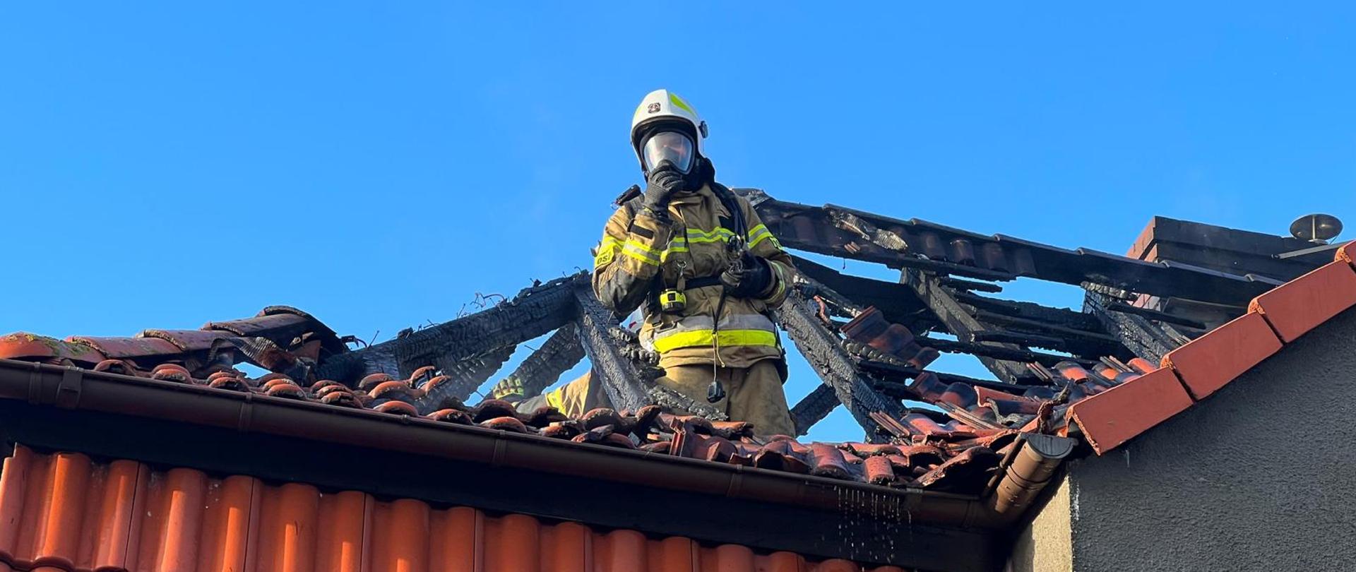 Zdjęcie przedstawia strażaka w aparacie ochrony układu oddechowego na spalonym poddaszu budynku.