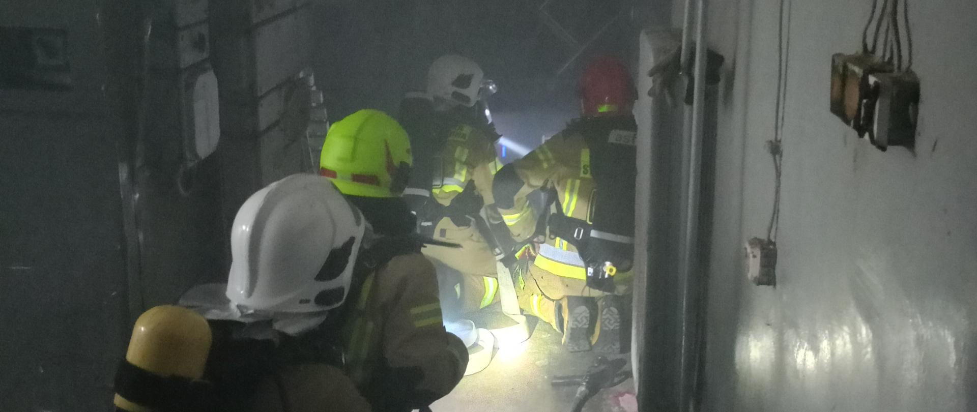 4 strażaków w zadymieniu w ubraniach bojowych koloru piaskowego. 