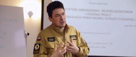 Komendant Centralnej Szkoły PSP podczas wystąpienia, w tle ekran multimedialny z wyświetlonym slajdem prezentacji
