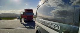 Na pierwszym planie (od prawej): bok oznakowanego furgonu dolnośląskiej Inspekcji Transportu Drogowego. W tle: przód zatrzymanego do kontroli zespołu pojazdów. Obok kabiny ciężarówki stoją umundurowani funkcjonariusze Inspekcji Transportu Drogowego.
