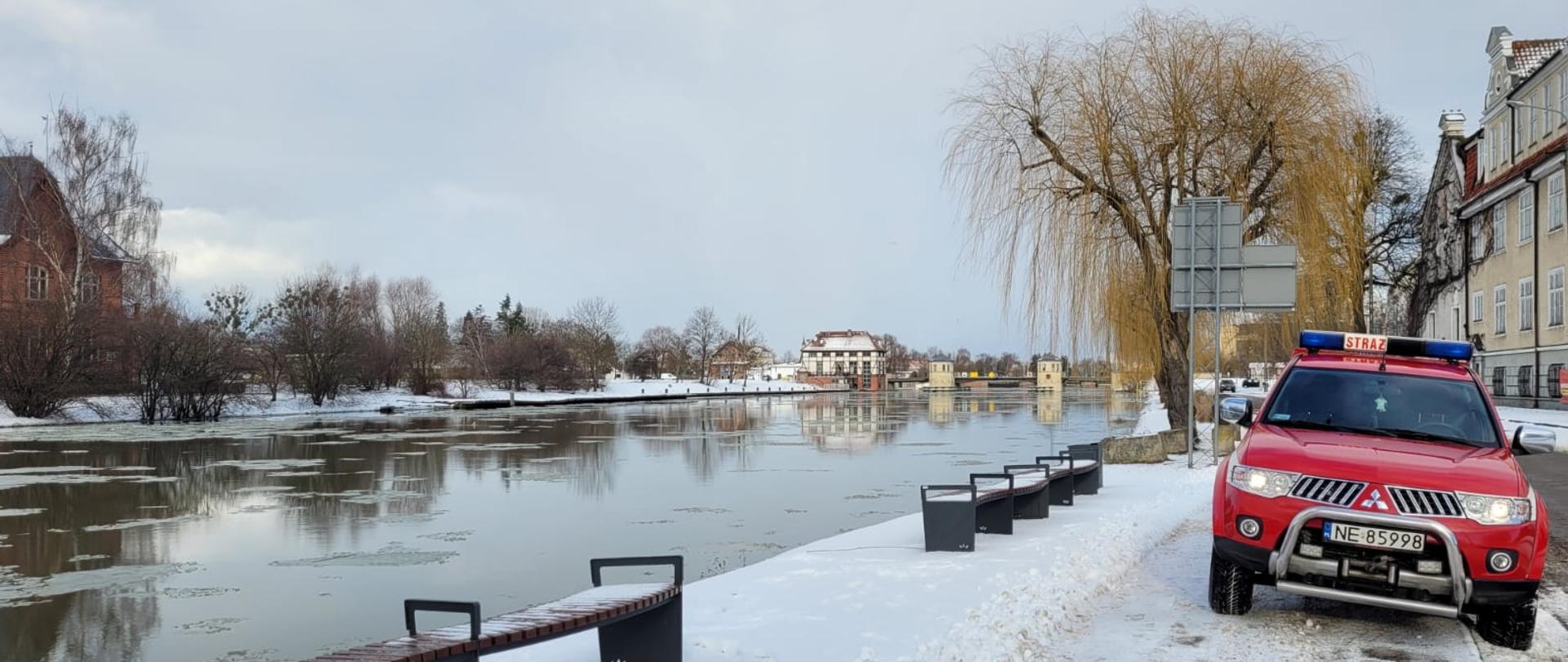 W centralnej części zdjęcia widoczny lekki samochód rozpoznania operacyjnego, po lewej stronie wysoki stan rzeki Elbląg. W tle widoczny Bulwar Zygmunta Augusta w Elblągu.