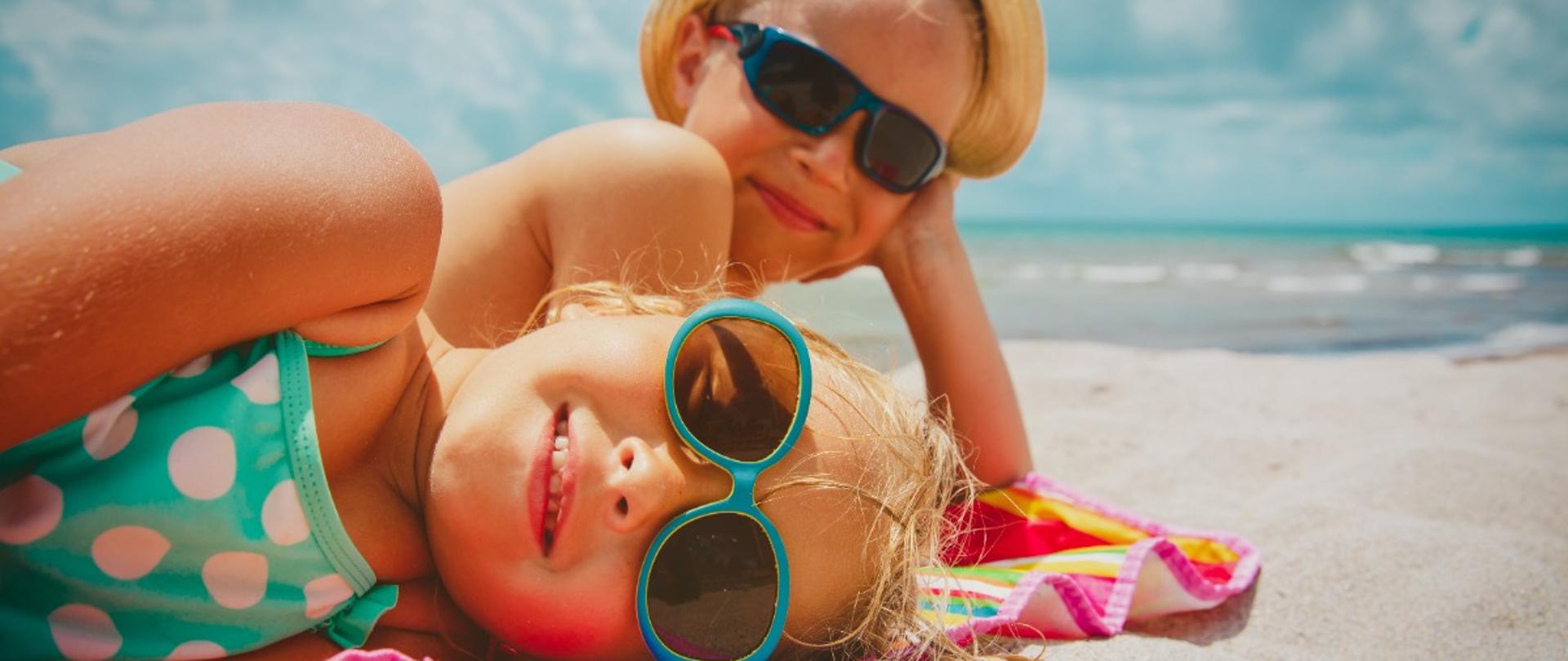 Dwoje dzieci w okularach przeciwsłonecznych, leży na plaży