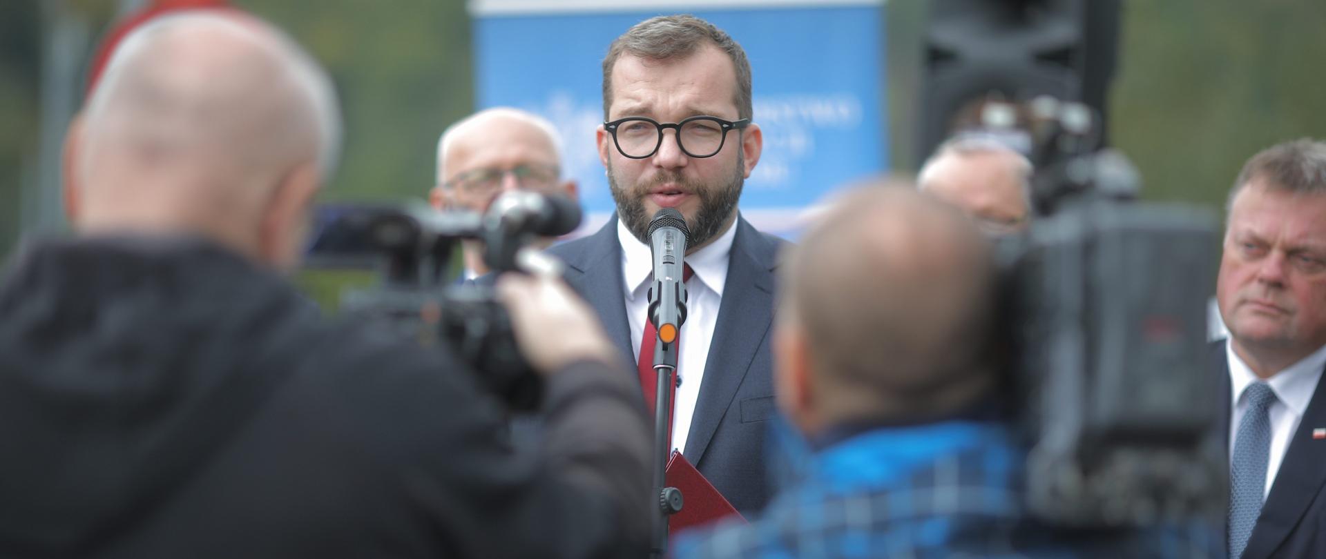 wiceminister Grzegorz Puda przemawia do mikrofonu, za nim samorządowcy
