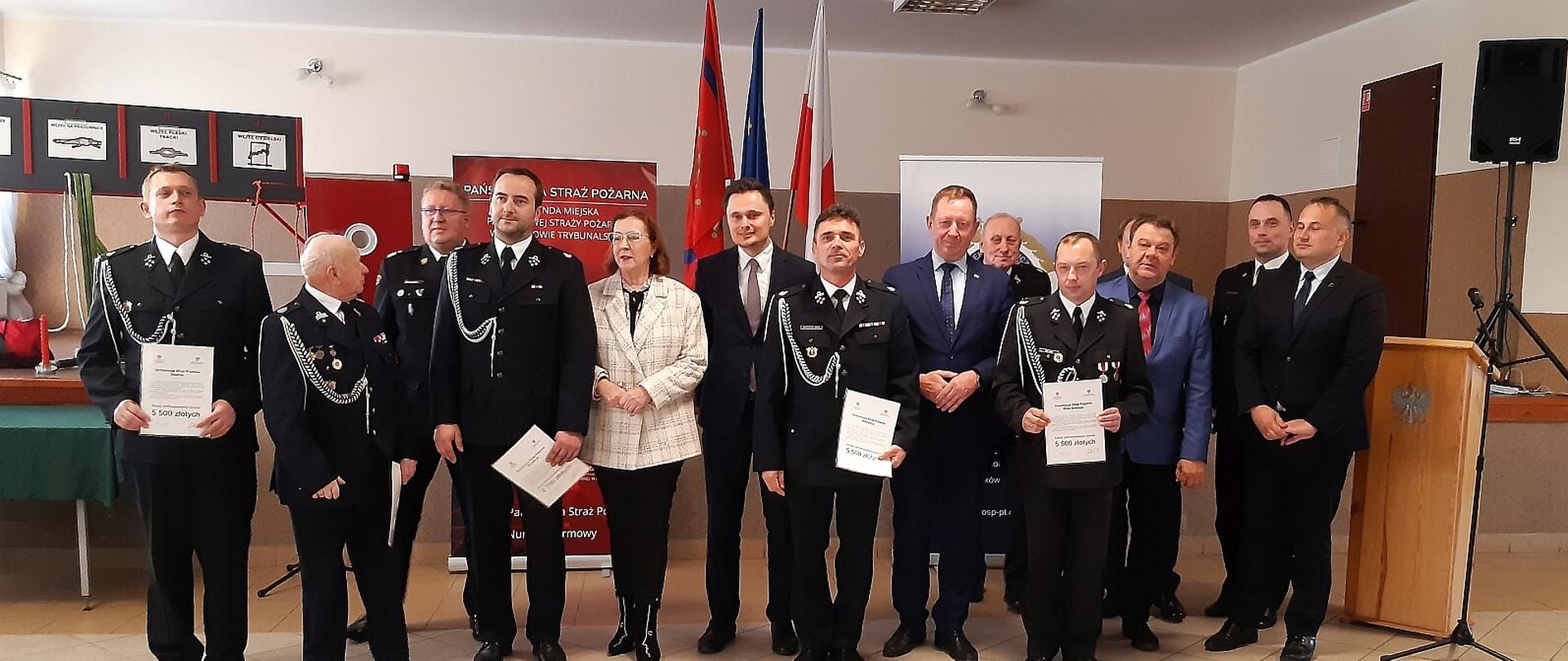 Przedstawiciele drużyn MDP z terenu powiatu radomszczańskiego pozują do zdjęcia z promesami. Na zdjęciu widoczne osoby, które wręczały promesy.