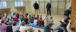Na zdjęciu widać funkcjonariusza PSP oraz policji ubranego w ubranie służbowe w trakcie pogadanki dla uczniów szkoły
podstawowej oraz przedszkola. Znajdują się na sali.