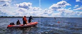 Zdjęcie przedstawia strażaków podczas ćwiczeń na zbiorniku Jeziorsko, którzy są na pontonie i podpływają do osoby znajdującej się w wodzie. Strażak z pontonu rzucił tzw. rzutkę ratowniczą w kierunku osoby znajdującej się w wodzie. 