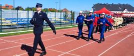 Na zdjęciu widoczny Komendant Gminny OSP z Gminy Radłów dh Michał Sekuła wprowadzający uczestników zawodów na stadion. Za nim idzie poczet flagowy oraz poszczególne drużyny.