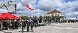 Moment podniesienia białoczerwonej flagi przyczepionej do kosza drabiny> pod nia stoi poczet flagowy i salutultuje, odgrywany jest hymn Polski. W tyle na truybunie honorowej stoja komendanci PSP innych słuzb oraz zaproszeni goście. Po prawej widac miszkańców i turystów obserwujacych uroczystosć