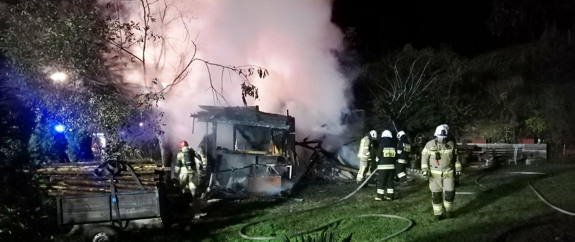 Dym unoszący się z garażu oraz strażacy prowadzący działania.