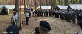 Strażący rozmowiają z młodzieża w leśnym obozowisku.