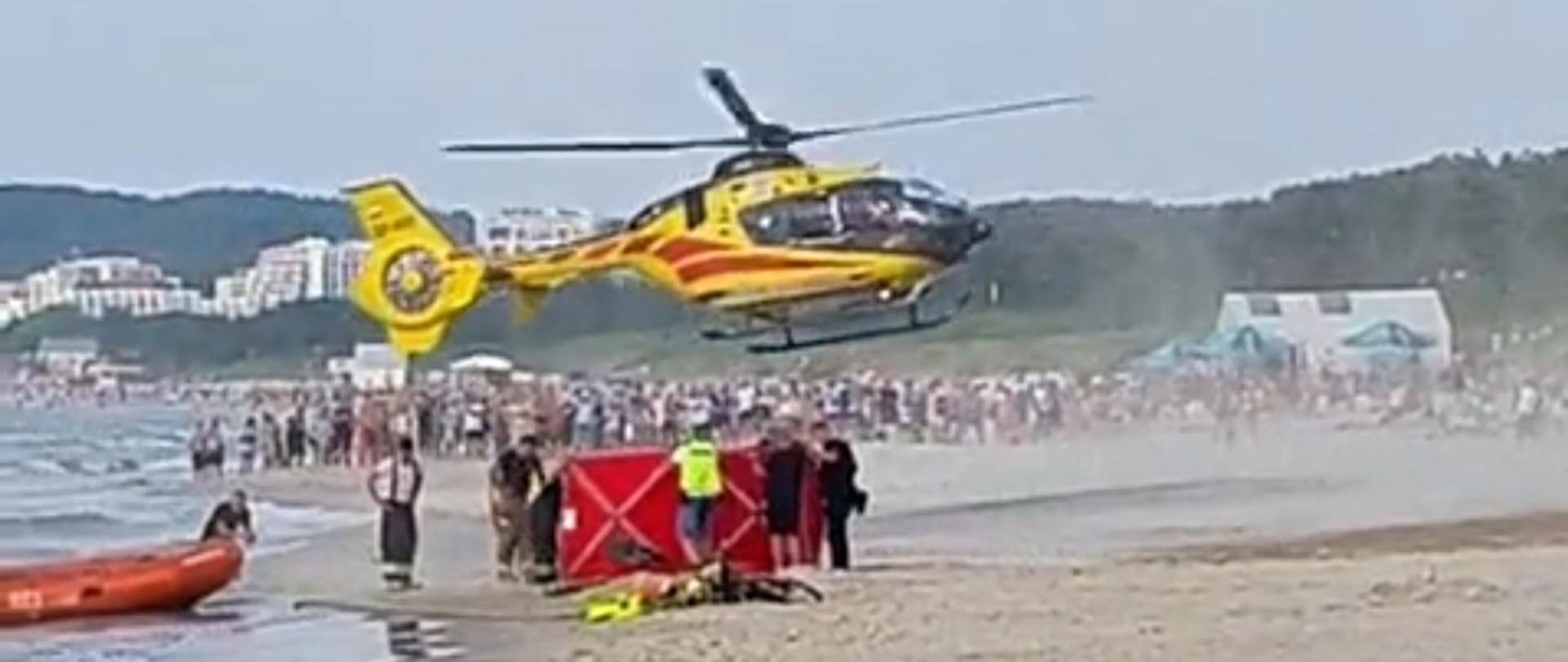 Zdjęcie przedstawia helikopter startujący na plaży w czasie akcji ratowniczej.