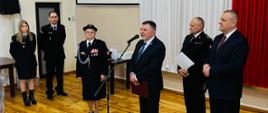 Poseł Andrzej Kryj przemawia do zgromadzonych strażaków OSP. Obok niego znajduje się wyróżniona Pani Krystyna Nowak, Burmistrz gminy Kunów i funkcjonariusze PSP