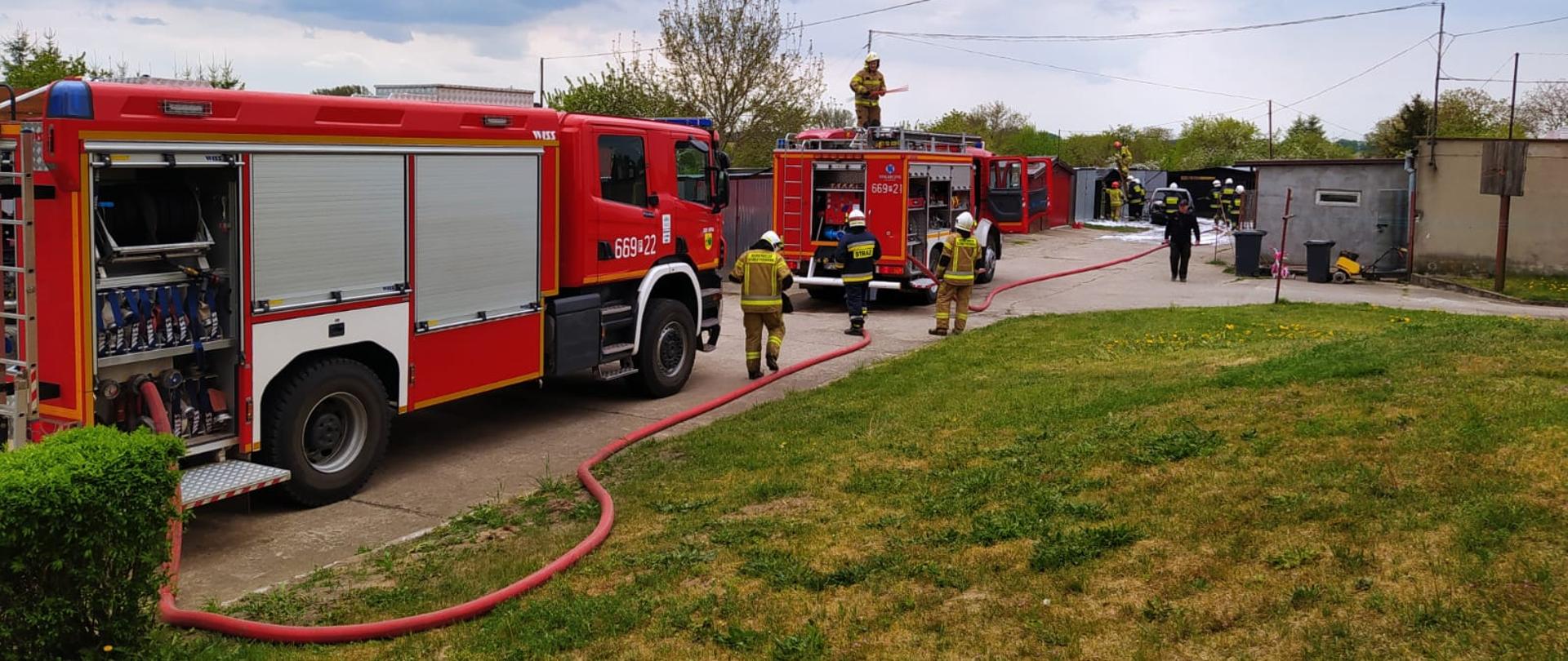 Na zdjęciu widoczne są samochody strażackie obok samochodów są strażacy którzy gaszą pożar