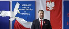 minister Przemysław Czarnek przemawia do mikrofonu podczas akcji szkoła do hymnu. w tle godło, biały orzeł oraz flaga Polski