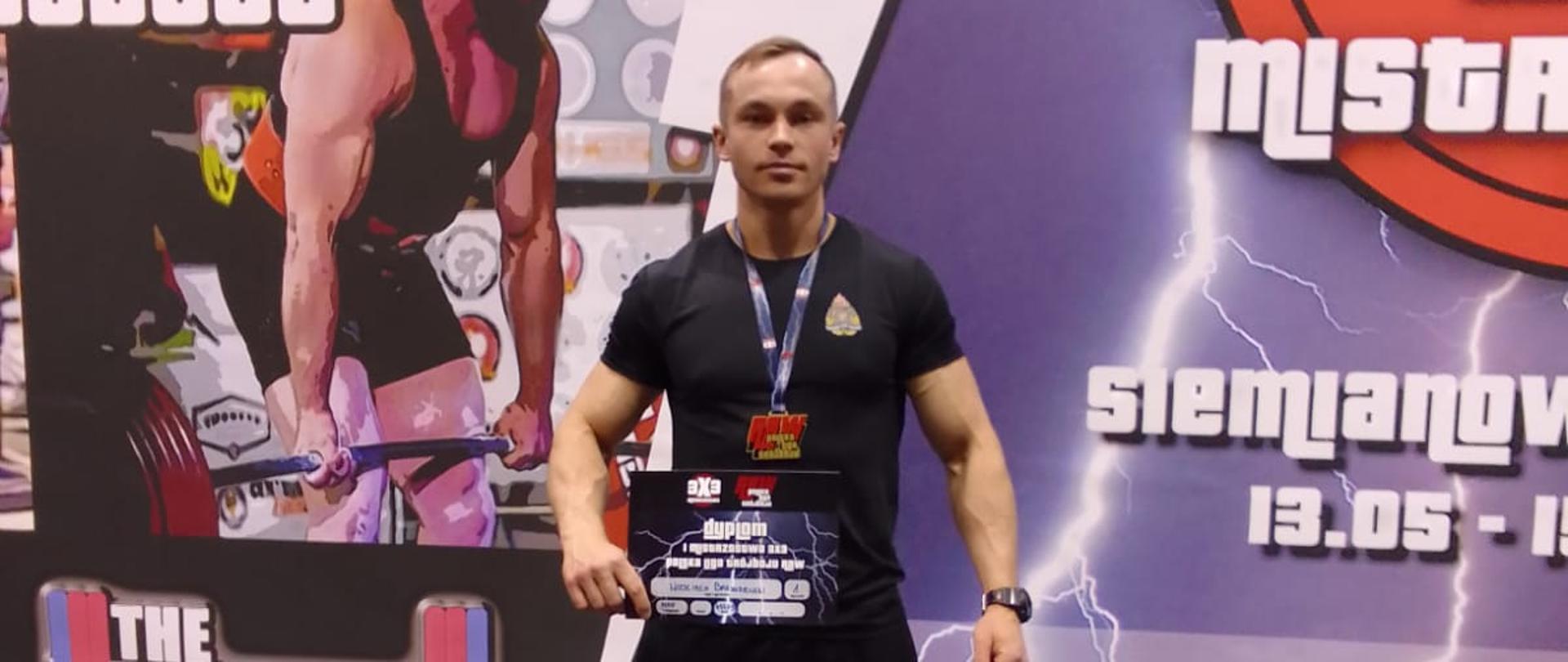 Funkcjonariusz pozuje na bilbordzie z dyplomem w ręku.