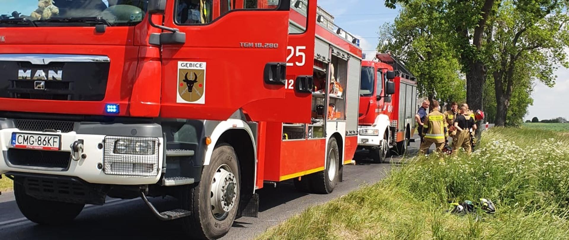 2 pojazdy pożarnicze i stojący obok strażacy