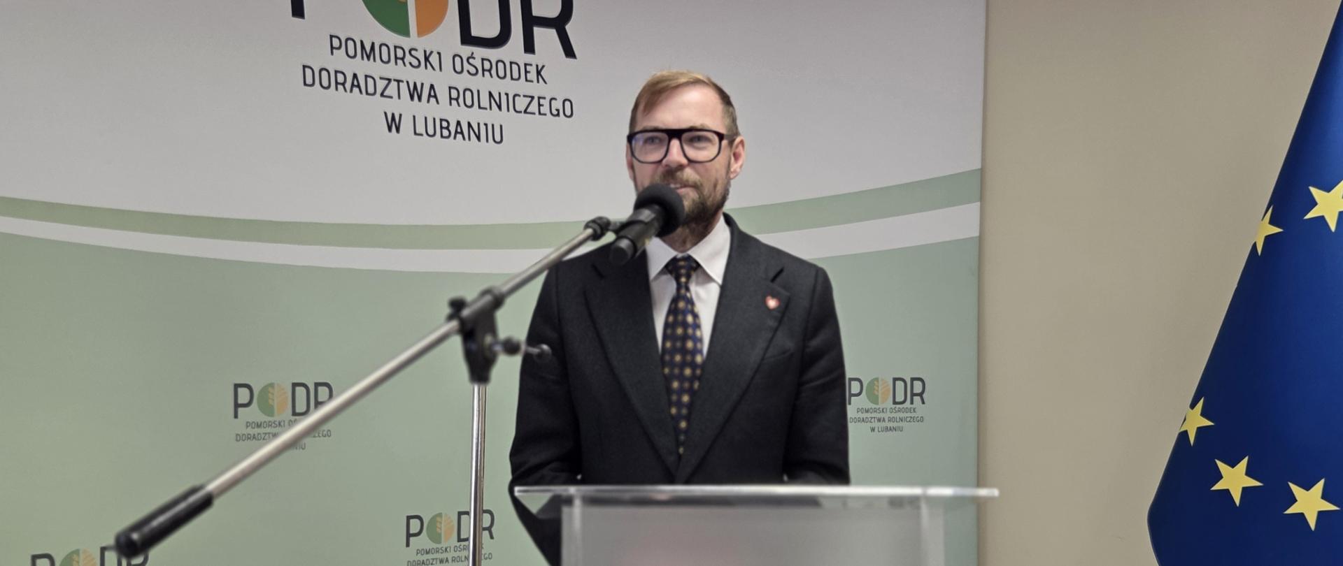 Mężczyzna w garniturze stoi przy mikrofonie na mównicy