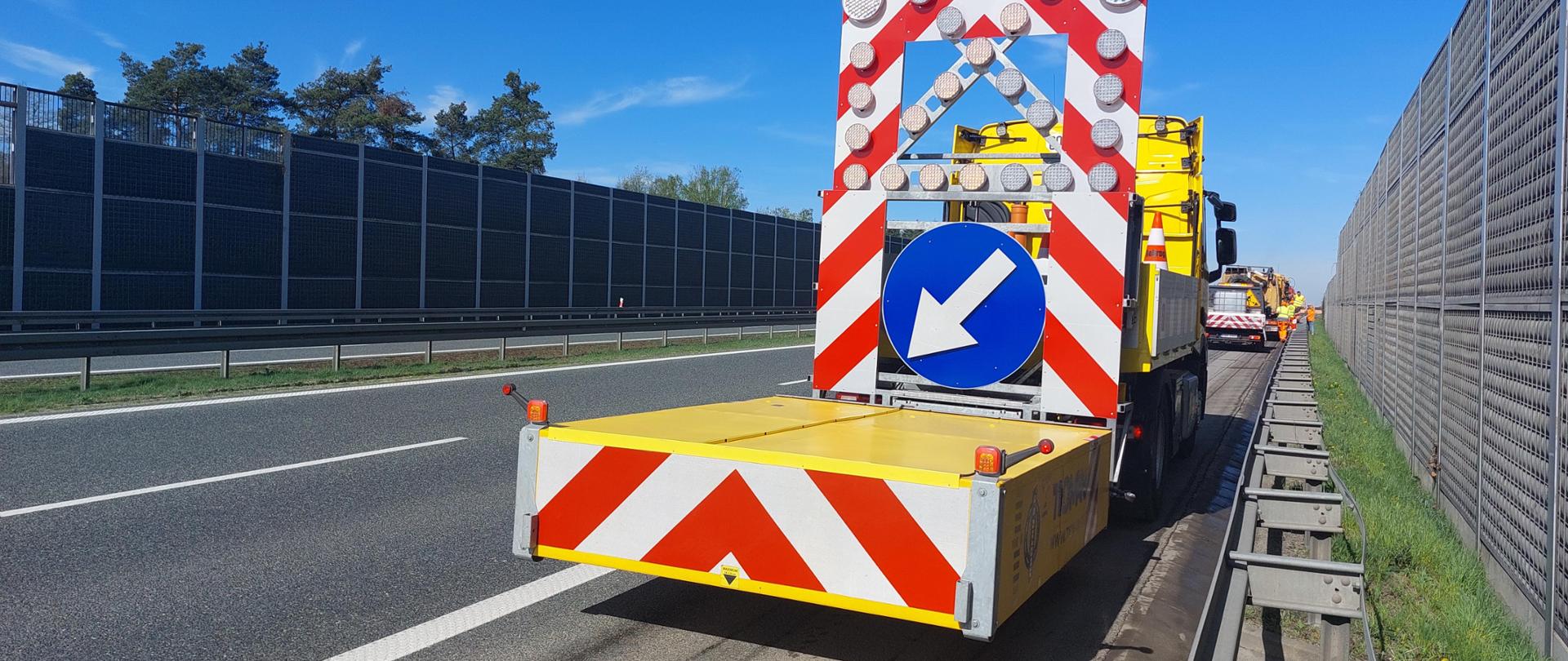 Zdjęcie przedstawia kolumnę aut służby drogowej, która sprawdza i czyści pobocza