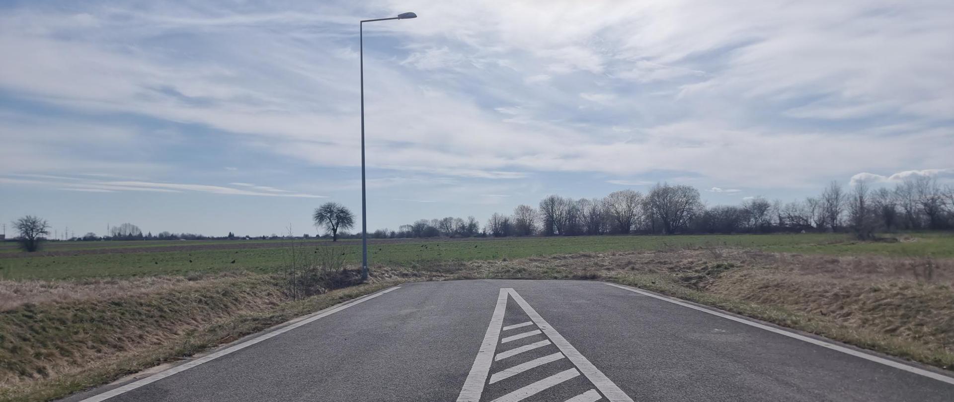 Odcinek drogi z pasem wyłączonym z ruchu na tle pól i nieba