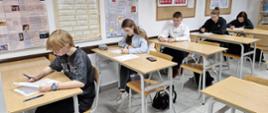Uczniowie siedzący w szkolnych ławkach rozwiązują test.