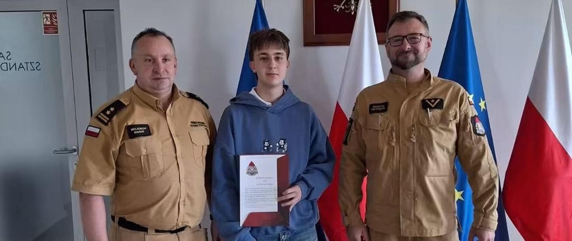 Na zdjęciu Komendant Powiatowy PSP w Pucku bryg. Wojciech Wanat oraz mł. asp. Marcin Pietrzak wręczają Julianowi Sępińskiemu list gratulacyjny za zdecydowane działanie podczas pożaru w Helu.