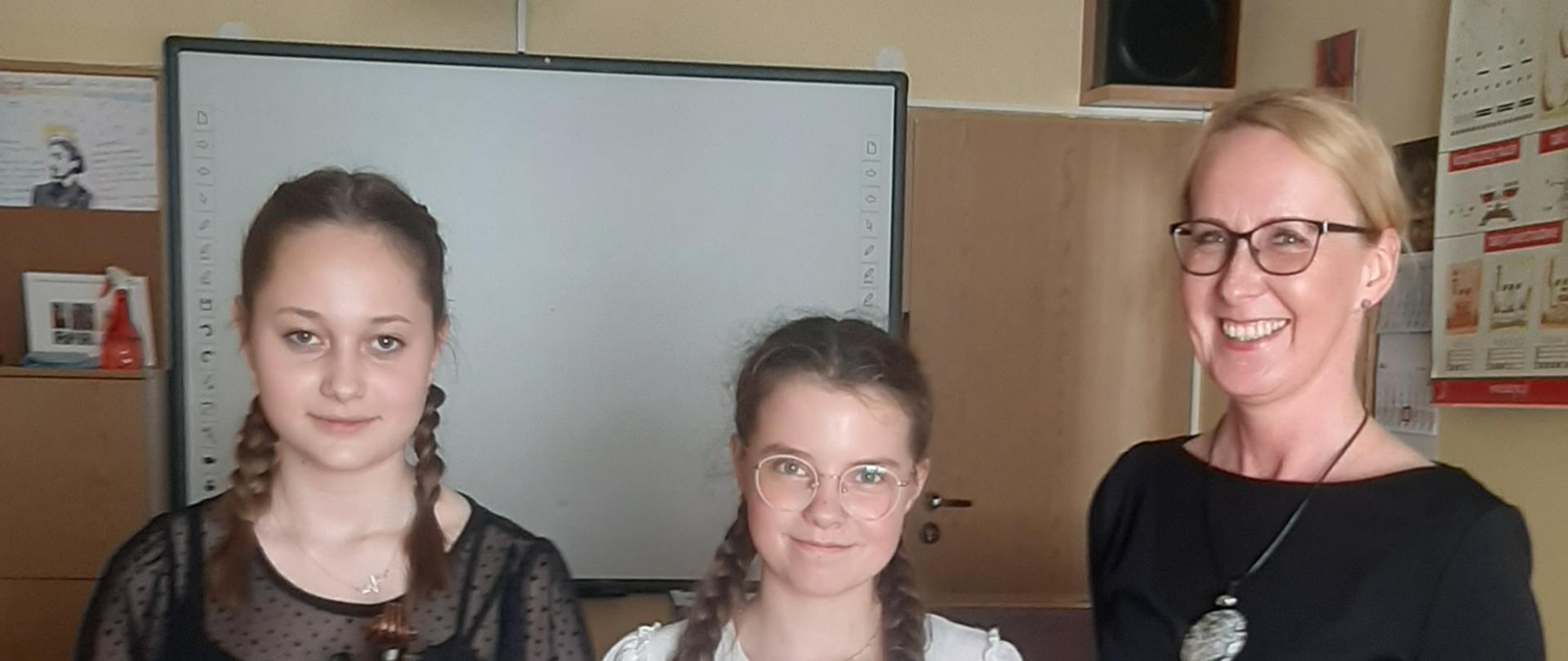 zdjęcie przedstawia uczennice szkoły. Uczennice stoją koło siebie od lewej strony i trzymają skrzypce, z prawej strony nauczycielka instrumentu głównego- skrzypce.