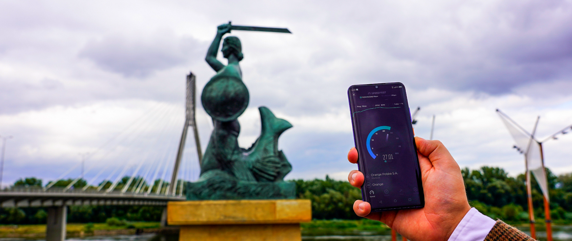 Telefon komórkowy, w tle pomnik warszawskiej syrenki oraz most Świętokrzyski