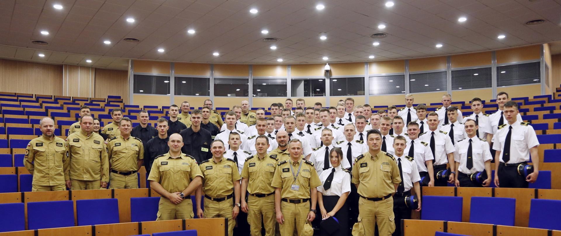 Aula Centralnej Szkoły PSP grupowe zdjęcie kadetów XXVI turnusu Dziennego Studium Aspirantów PSP wraz z Komendantem Centralnej Szkoły PSP jego zastępcą oraz kadrą wydziału nauczania Centralnej Szkoły PSP