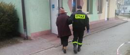 zdjęcie przedstawia strażaka OSP pomagającego osobie starszej w dotarciu do punktu szczepień 