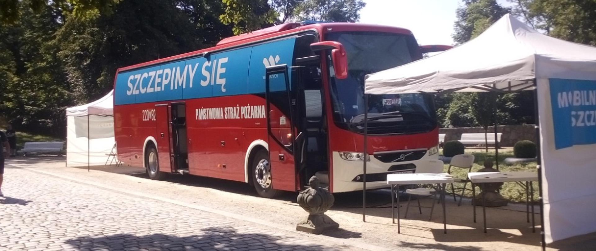 Czerwony autobus straży pożarnej z niebieskim napisem szczepimy się stoi na parkingu