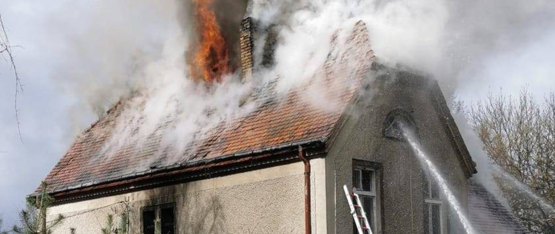 Budynek z widocznym słupem ognia wydostającym się z pod kalenicy 