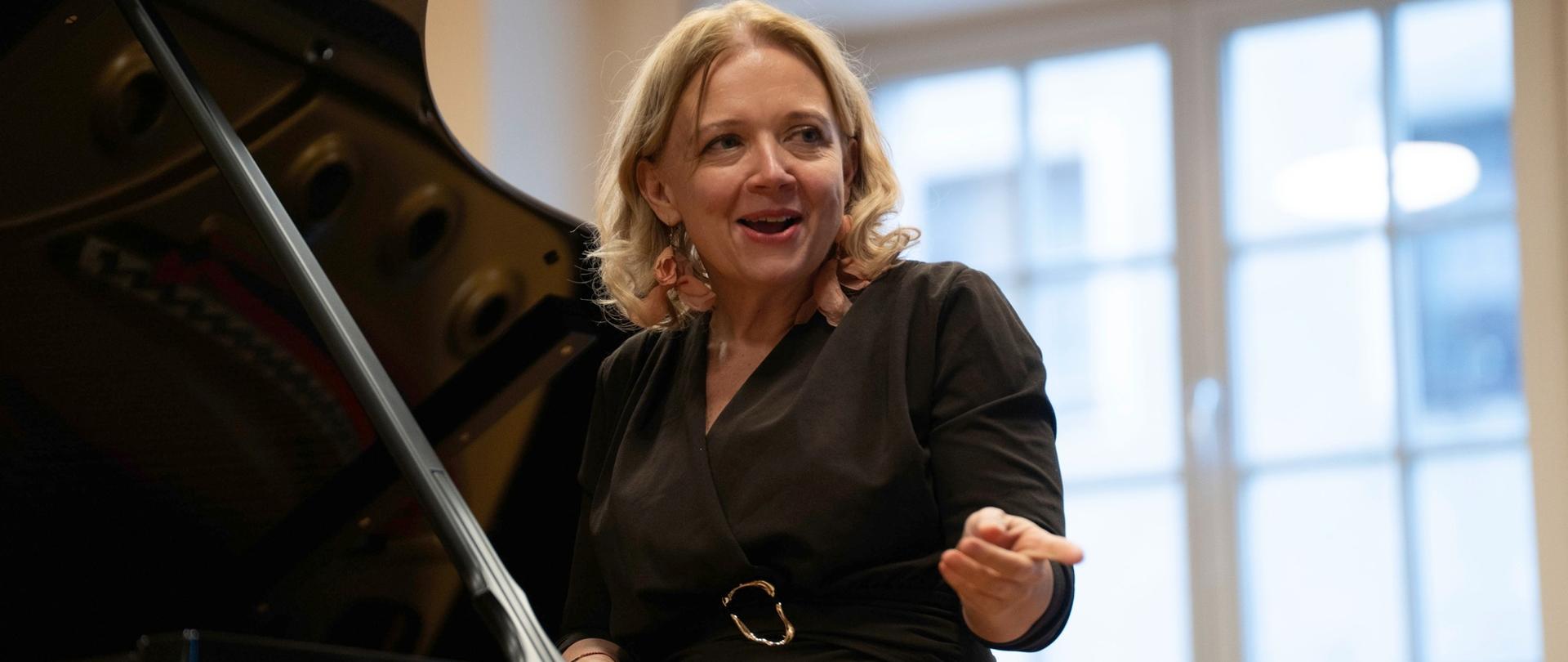 zdjęcie przedstawia prowadzącą warsztaty przemawiającą do publiczności przy podniesionym skrzydle fortepianu na scenie sali koncertowej, inne ujęcie z bliska