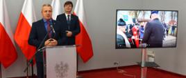 
Mężczyźni w garniturach w sali konferencyjnej, obok telewizor