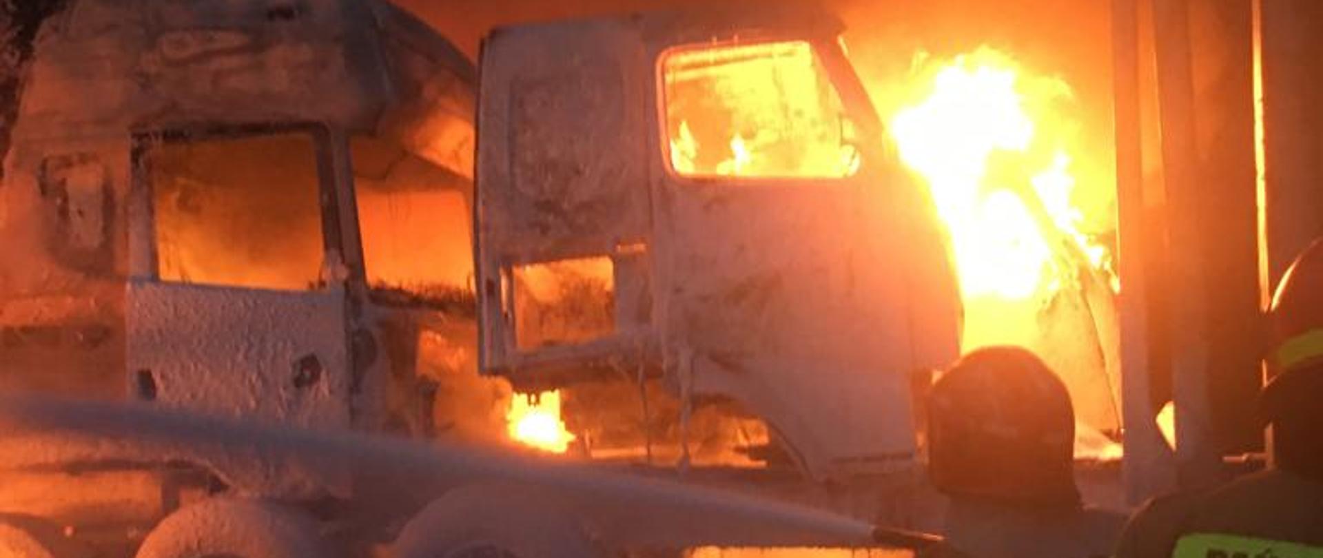 Strażacy prowadzą akcję gaśniczą palących się naczep ciężarowych na których składowane były kabiny ciągników siodłowych po demontażu. Pożar jest w bardzo rozwiniętej fazie. Strażacy używają piany ciężkiej do gaszenia pożaru.