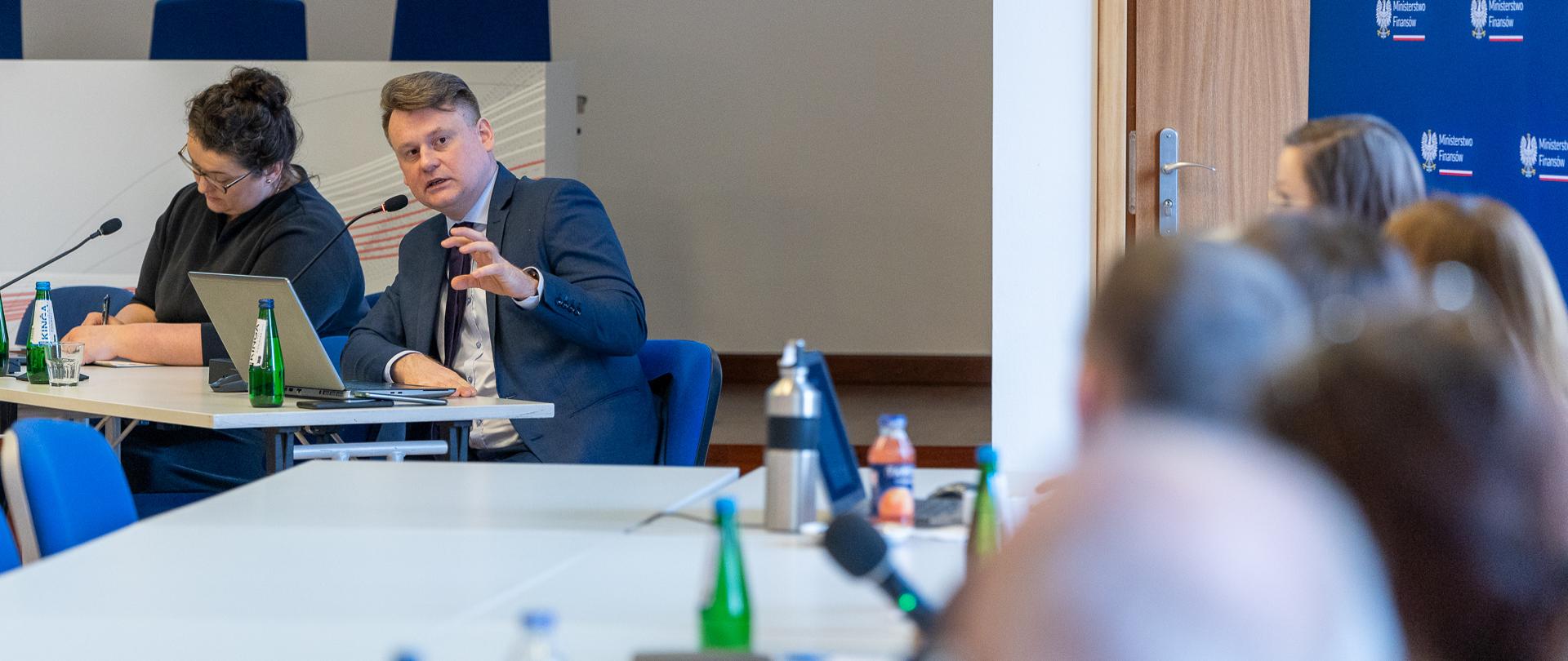 Uczestnicy spotkania siedzą w sali konferencyjnej, na stołach mikrofony i komputery