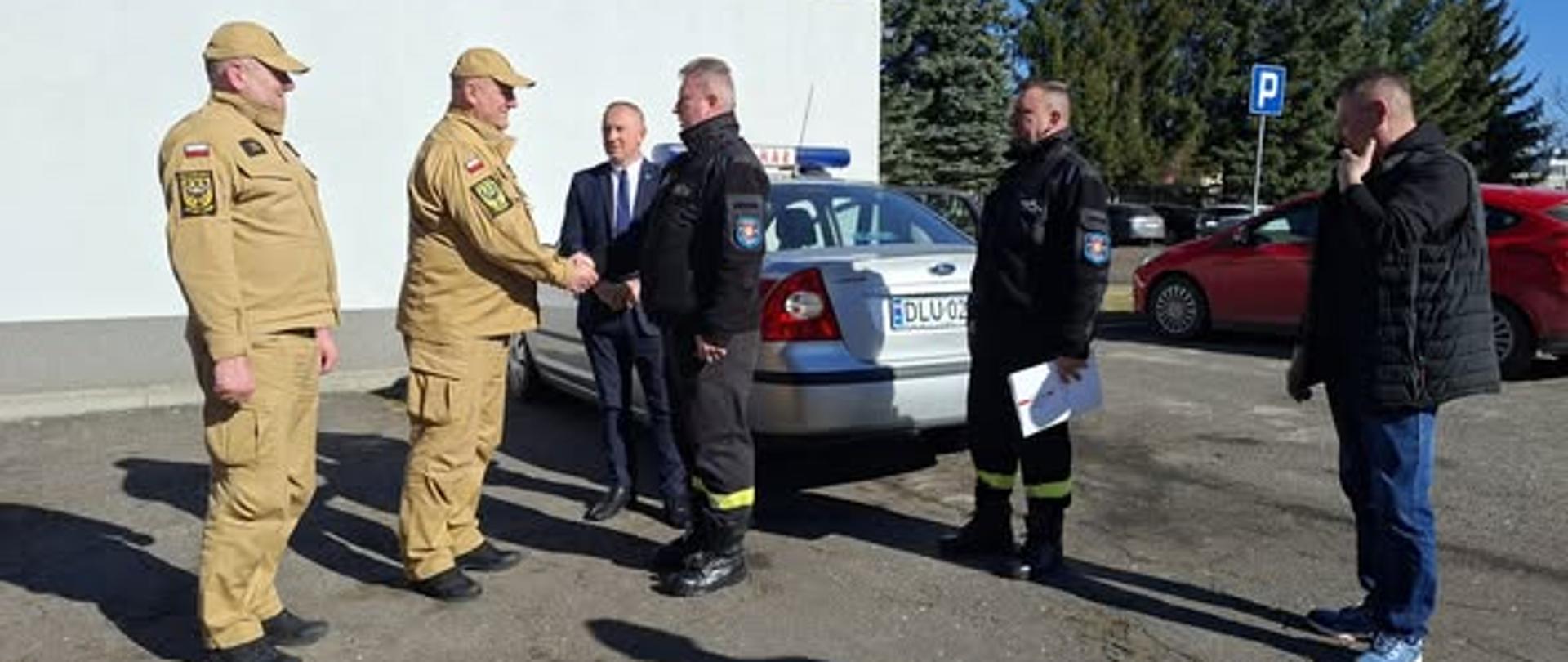 Zdjęcie przedstawia moment przekazania samochodu operacyjnego z Komendy Powiatowej PSP w Lubinie do OSP Chobienia. Przekazanie odbywa się na placu wewnętrznym Komendy Powiatowej PSP w Lubinie.