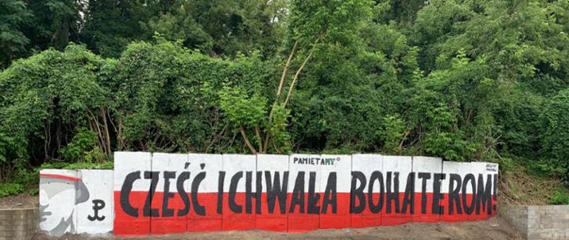 Na zdjęciu widoczny czarny napis na biało-czerwonych barwach "Cześć i Chwała Bohaterom"