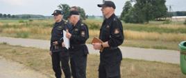 Ćwiczenia "Plutonu Rawicz". Teren nad zbiornikiem retencyjnym w Jutrosinie. Funkcjonariusze z Komendy Powiatowej PSP w Rawiczu przeprowadzają odprawę ze strażakami przybyłymi na ćwiczenia.
